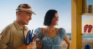João Gomes e Bruna Marquezine aparecem sorridentes em um quiosque de praia, observando sandálias enquanto seguram chinelos, em uma cena leve e descontraída que remete ao verão e ao lifestyle das Havaianas.