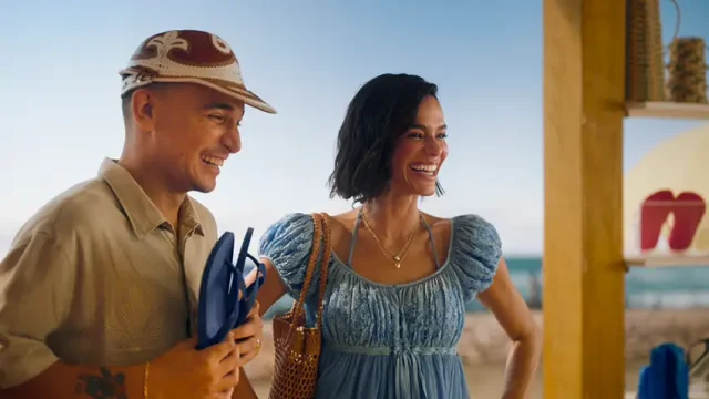 João Gomes e Bruna Marquezine aparecem sorridentes em um quiosque de praia, observando sandálias enquanto seguram chinelos, em uma cena leve e descontraída que remete ao verão e ao lifestyle das Havaianas.