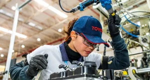 Funcionária da Toyota trabalha na montagem de motor em fábrica da empresa, destacando tecnologia e produção automotiva no Brasil.