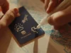 Campanha Itaú Personnalité mostra pessoa desenhando símbolos em cartão azul sobre papel, representando sonhos, projetos e conquistas financeiras.