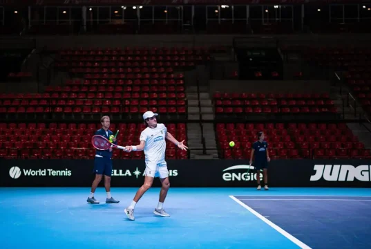 João Fonseca treina na quadra da Copa Davis, com arquibancadas ao fundo, durante preparação para o confronto entre Brasil e Suíça no Rio de Janeiro.