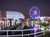 Rio Gastronomia 2026 no Jockey Club, com roda-gigante iluminada, espaços de marcas, área gastronômica e lago refletindo as luzes do evento.