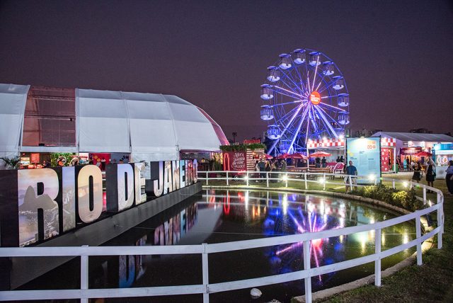Rio Gastronomia 2026 no Jockey Club, com roda-gigante iluminada, espaços de marcas, área gastronômica e lago refletindo as luzes do evento.