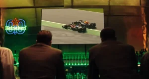 Heineken® 0.0 exibe corrida de Fórmula 1® em telão durante ação de marca, com iluminação verde, garrafas do produto e identidade visual da campanha.
