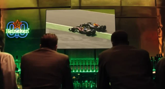 Heineken® 0.0 lança filme inspirado no universo da Fórmula 1® Heineken® 0.0 exibe corrida de Fórmula 1® em telão durante ação de marca, com iluminação verde, garrafas do produto e identidade visual da campanha.