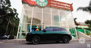 SUV Leapmotor C10 Ultra-Híbrido estacionado em frente ao Centro de Excelência da Academia de Futebol do Palmeiras, com a identidade visual do clube ao fundo.