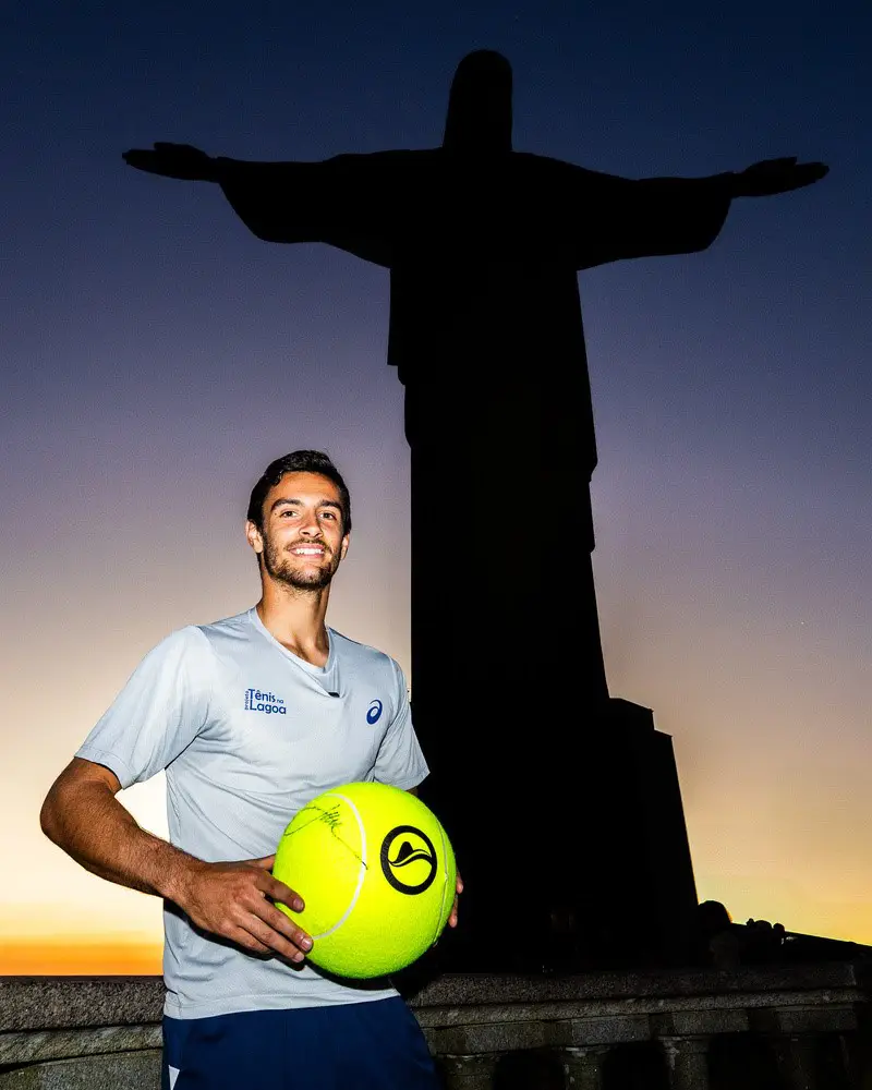 Tenista italiano Lorenzo Musetti posa com uma bola de tênis em frente à silhueta do Cristo Redentor, no Rio de Janeiro, durante a divulgação de sua participação no Rio Open 2027.