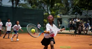 Menina pratica tênis em quadra de saibro durante atividade infantil do Rio Open, utilizando raquete e bola em exercício esportivo.