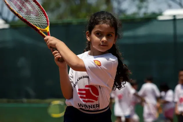 Menina participa de atividade de t&ecirc;nis do projeto Winners, segurando uma raquete durante exerc&iacute;cio em quadra de saibro.