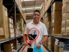 Ronaldo Fenômeno segura uma raquete de tênis HEAD e uma bolsa esportiva da marca em um depósito com produtos e caixas da fabricante.