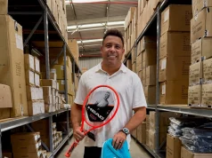 Ronaldo Fenômeno segura uma raquete de tênis HEAD e uma bolsa esportiva da marca em um depósito com produtos e caixas da fabricante.