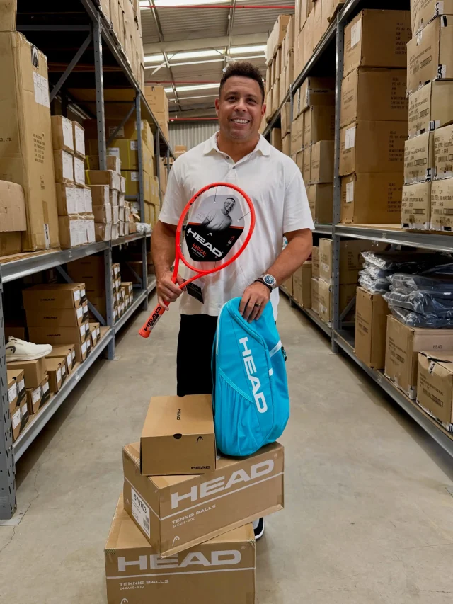 Ronaldo Fenômeno adquire controle da HEAD no Brasil e amplia investimentos no tênis Ronaldo Fenômeno segura uma raquete de tênis HEAD e uma bolsa esportiva da marca em um depósito com produtos e caixas da fabricante.